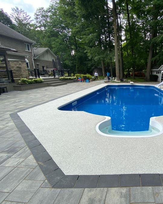A pearl-white Gator Grip pool deck with a charcoal border around an in-ground pool